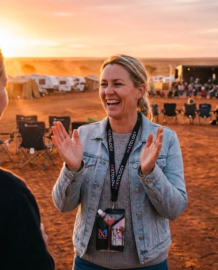 Festival-goer at golden hour on red dirt plains wearing a MXTOLOGY cocktail pouch on a lanyard