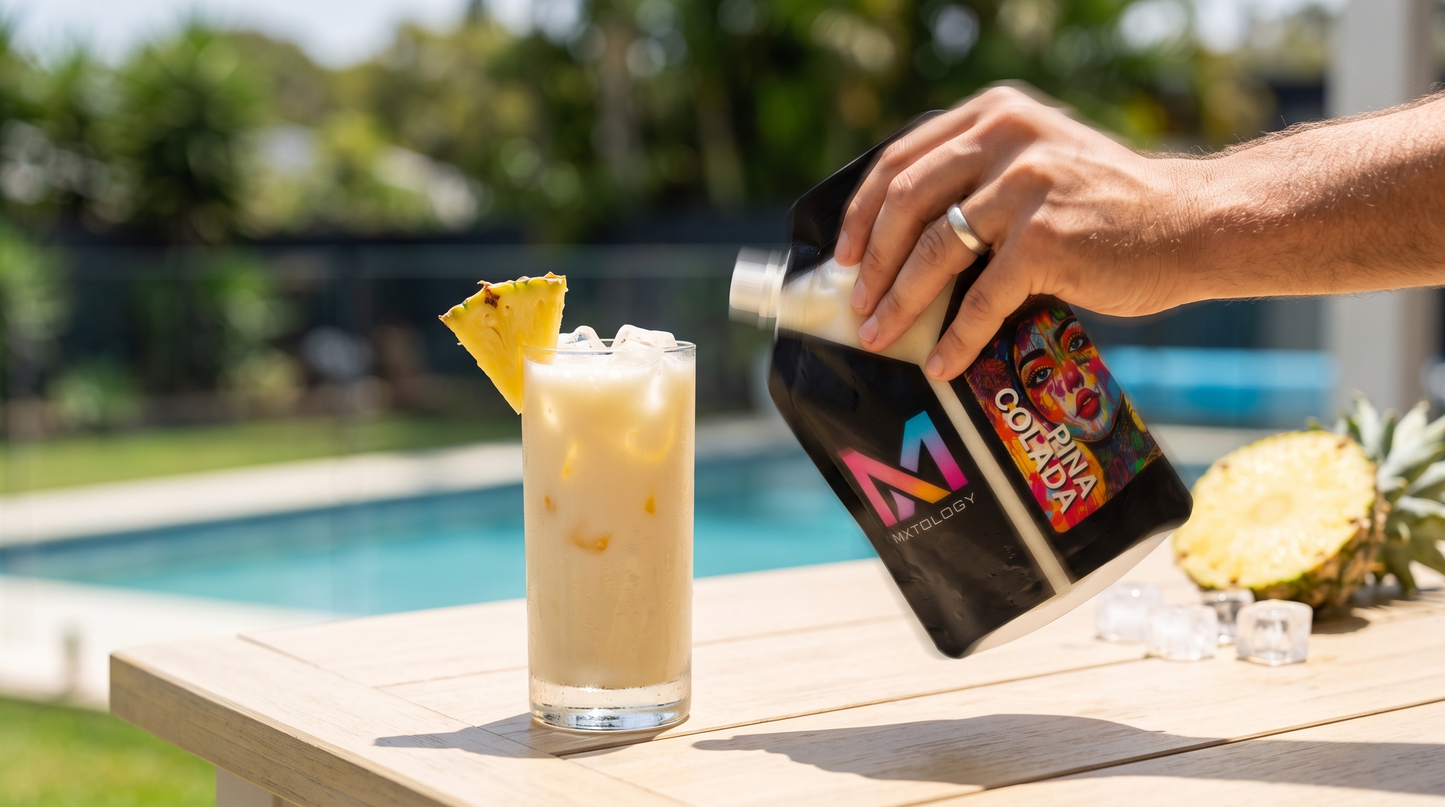 Hand shaking a MXTOLOGY Piña Colada cocktail pouch beside a poured Piña Colada over ice on a poolside table in Australia - no blender needed