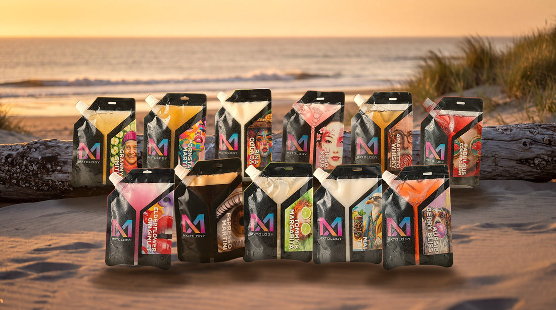 All 11 MXTOLOGY cocktail pouches lined up on driftwood on a beach at sunset
